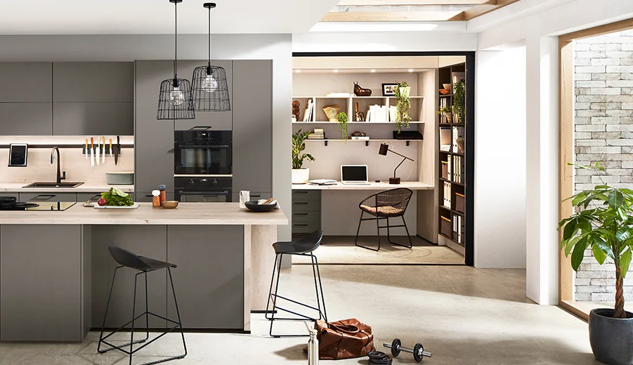Moderne offene Küche mit eleganten Schränken und einer Insel, die zu einem gemütlichen Homeoffice mit Bücherregalen führt, beleuchtet von natürlichem und Pendelleuchten.