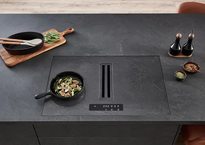 Modernes Kochfeld mit integriertem Dunstabzug auf einer Kücheninsel. Xtra Hob Lösung mit flächenbündiger Optik und eleganter Bedienleiste. Hochwertige Ausstattung für stilvolles Kochen.