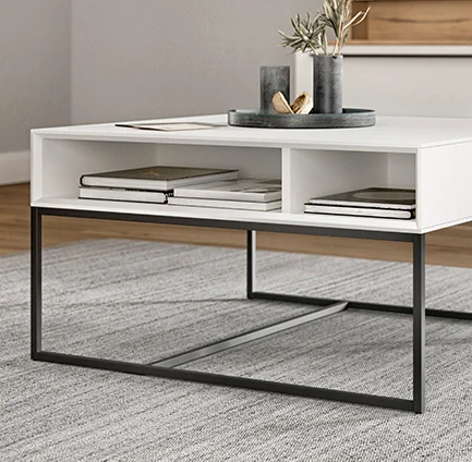 Minimalistischer weißer Couchtisch mit schlanken schwarzen Metallbeinen, der ein offenes Regal mit Büchern und Dekorationsgegenständen in einem modernen Wohnraum zeigt.