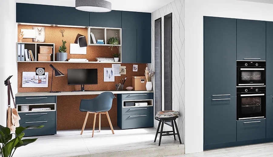 Modernes Homeoffice-Setup mit einem eleganten Schreibtisch, wandmontierten Regalen und einer Küchenzeile mit dunkelblauen Schränken und eingebauten Geräten.