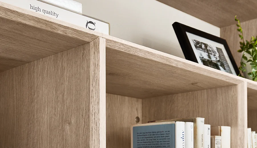 Elegante Holzregale zeigen verschiedene Bücher, ein gerahmtes Foto und eine dekorative Schachtel mit einem Etikett "hochwertig", was auf einen anspruchsvollen und organisierten Raum hinweist.