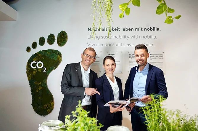 Drei Personen vor einem begrünten CO₂-Fußabdruck und dem Schriftzug „Nachhaltigkeit leben mit nobilia“