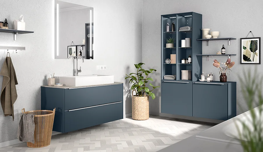 Modernes Badezimmer mit marineblauen Schränken, einem eleganten Spiegel und dekorativem Grün, das ein sauberes und stilvolles Design präsentiert.