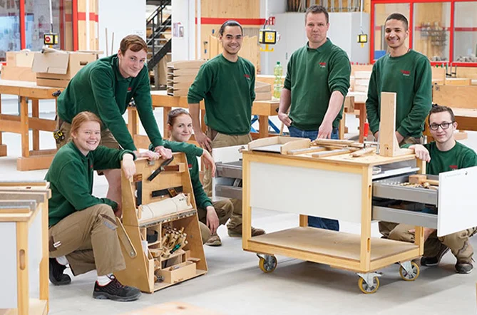 nobilia Auszubildende mit Möbelbauteilen und Werkzeug an Werkbänken in einer Werkstatt