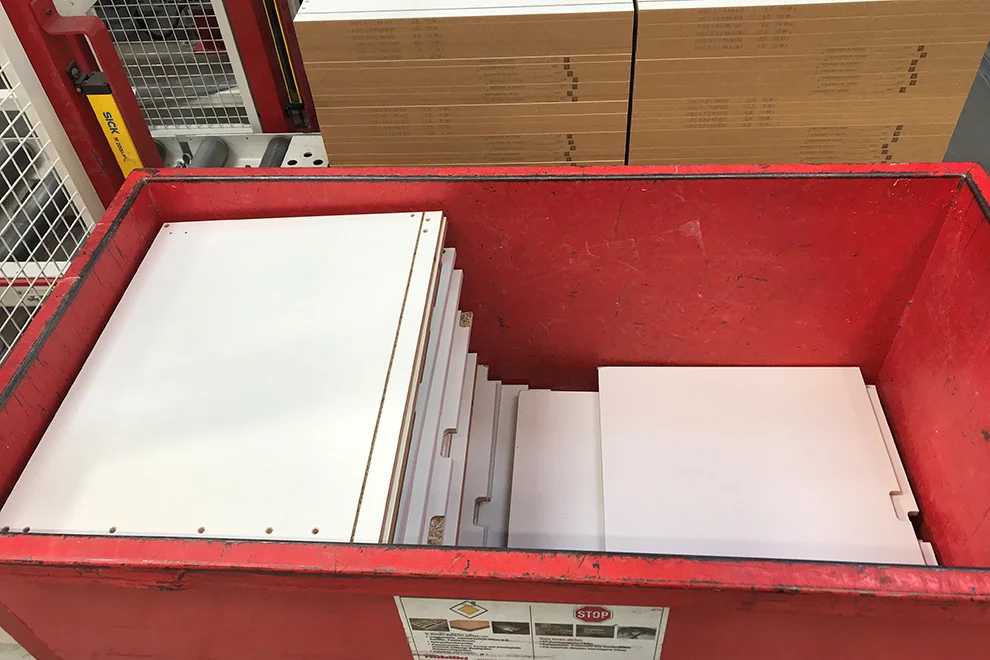 Stapel flach verpackter Möbelstücke, die in einem roten Metallbehälter organisiert sind und bereit für die Montage oder den Transport sind, gesehen in einem Lagerumgebung.